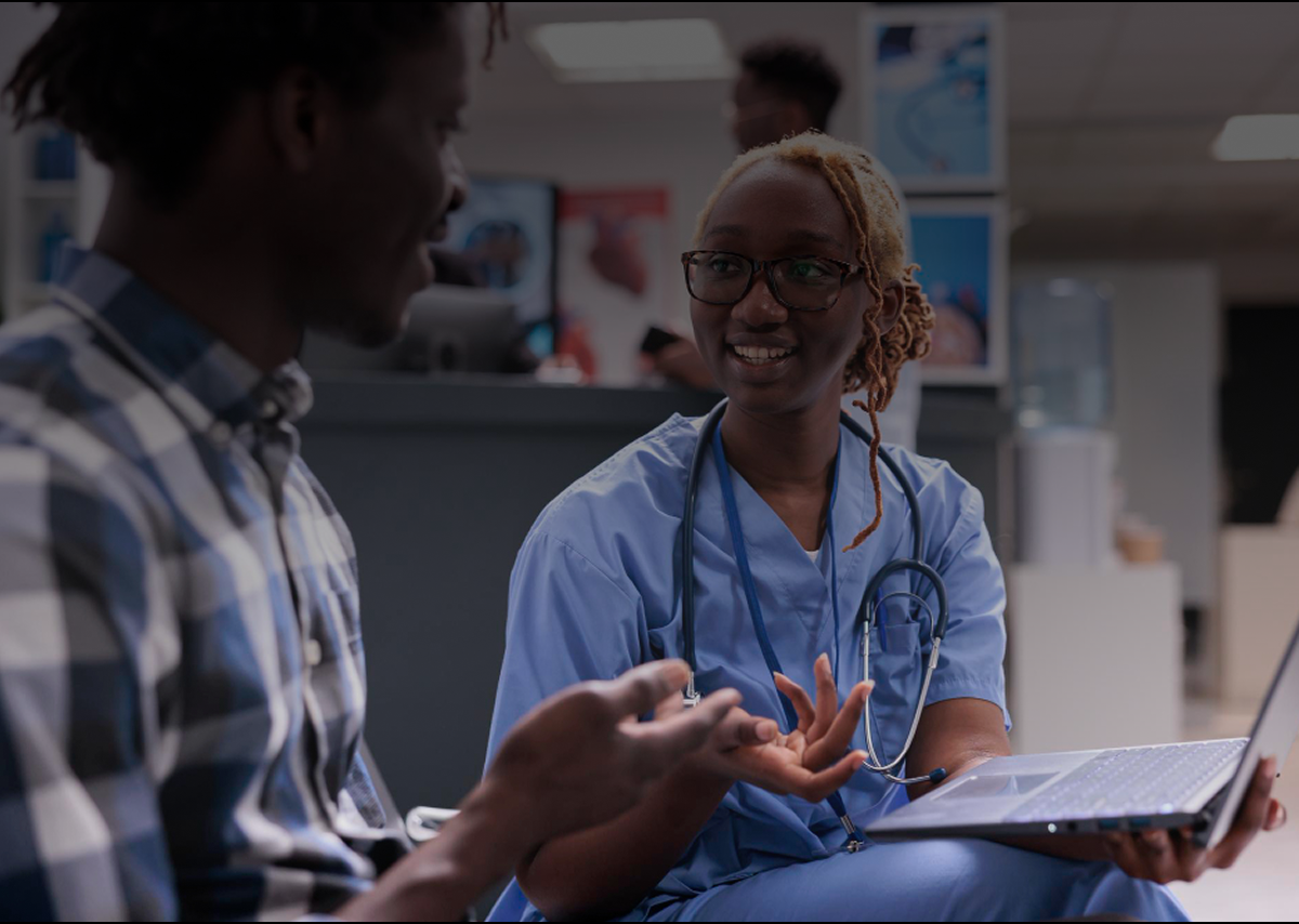 A nurse with a laptop talking with a patient in a clinic waiting area