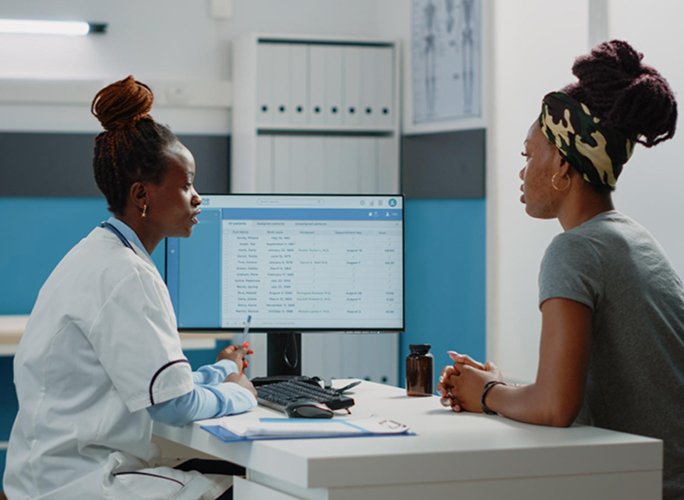 A clinician at a desk talking with a patient during a consultation